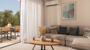 A modern living room with a sofa, a round table with a vase, and a view through a large window. - Cossoro Cave Villa Vasilikos (Vasilikos)