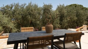 An outdoor dining area with a table and chairs, a large woven vase, and a backdrop of dense foliage. - Cossoro Cave Villa Vasilikos (Vasilikos)