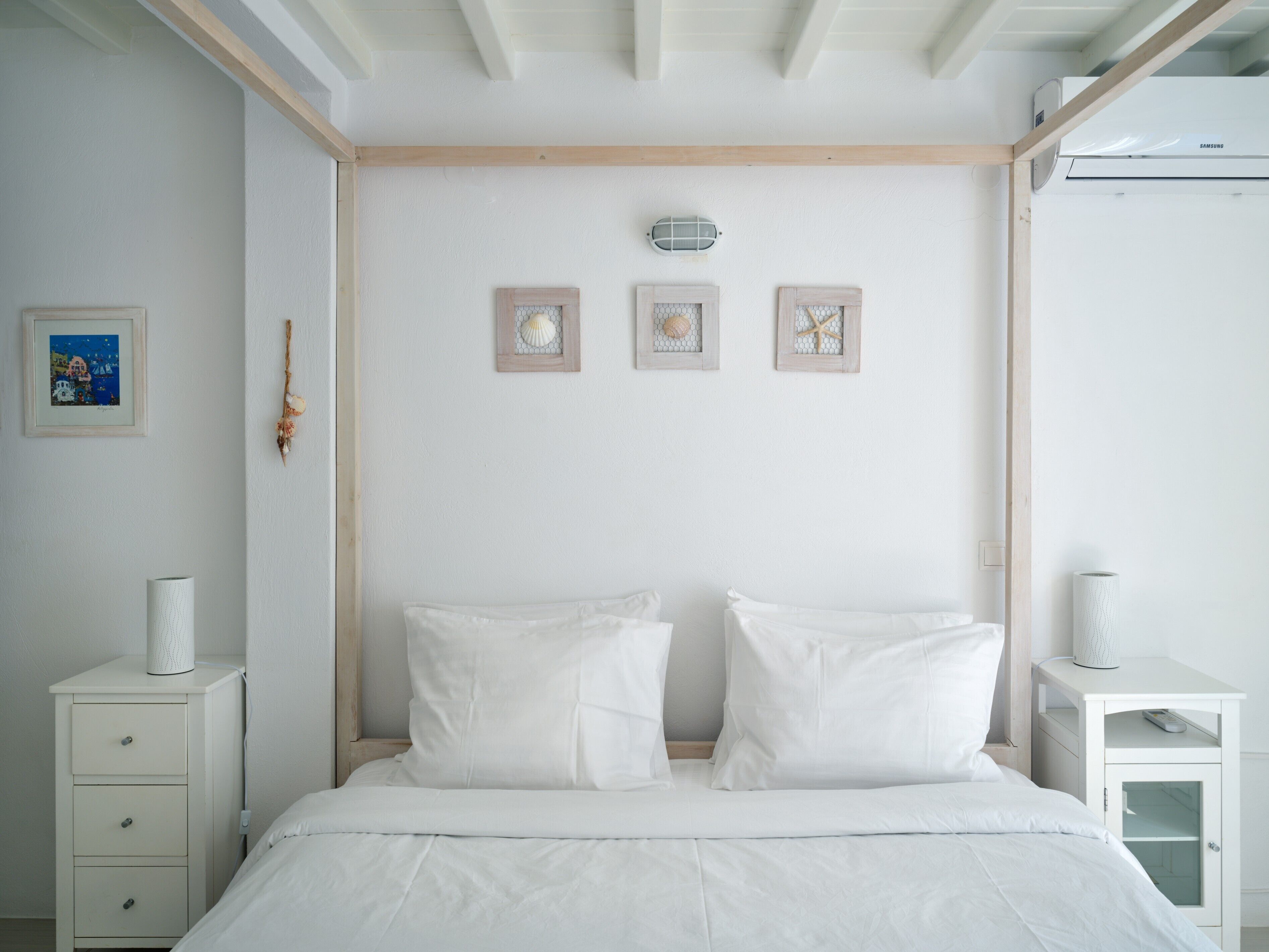 A bedroom with a bed, two bedside tables, a wall-mounted air conditioner, and three framed pictures.