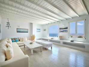 A spacious living room with a white sofa, a coffee table, and a view of the sea through large windows. - Blue Lounge Villa, Mykonos – Stunning Views & Private Pool (Mykonos)
