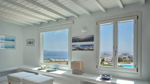 Habitación con un amplio ventanal que ofrece vista al mar y un banco blanco con un cuenco y objetos decorativos.