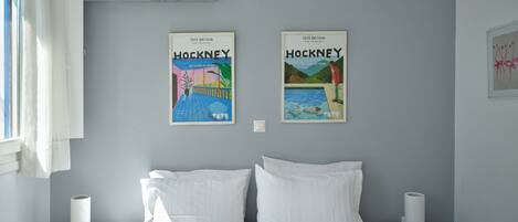 A bedroom with a bed, two nightstands, a window with curtains, and two framed posters on the wall.