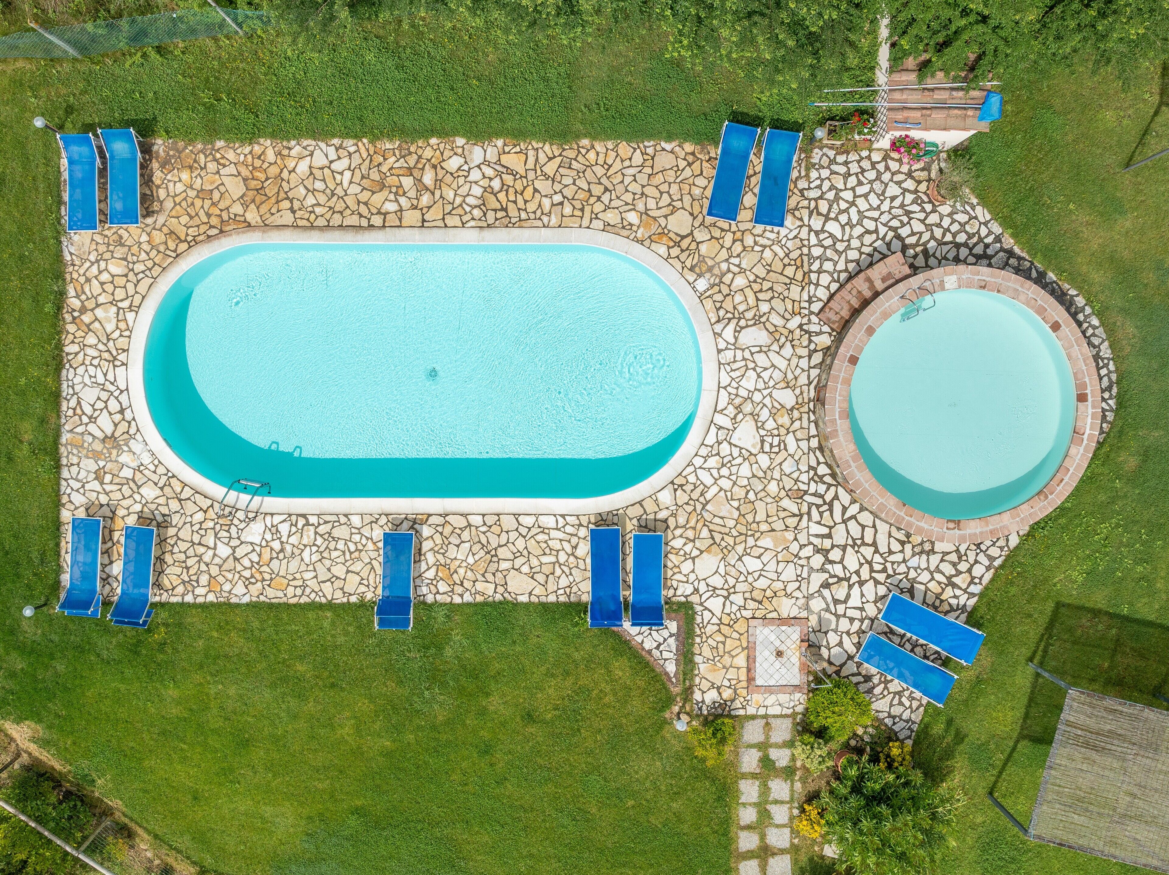 An aerial view of a rectangular swimming pool with a stone border, surrounded by a stone patio, and four blue lounge chairs.