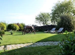 A well-maintained lawn with a swing set, two lounge chairs, and a stone wall in a garden setting.