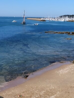 Una playa con agua cristalina, barcos y un litoral rocoso.