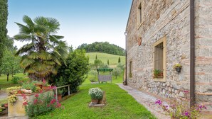 Un edificio in pietra con un giardino antistante, inclusi un'area palme e diverse piante in vaso.