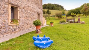 Un edificio in pietra con un cortile erboso, una barca gonfiabile blu e una struttura in legno con un camino.