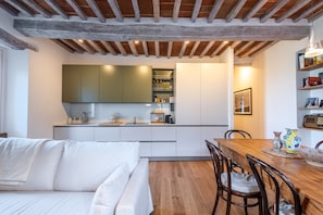 Una cucina moderna con mobili bianchi, un tavolo da pranzo in legno e un'area salotto accogliente con un divano bianco.