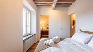 Een slaapkamer met een bed, opgerolde handdoeken, een radiator, een houten plafond en een raam.