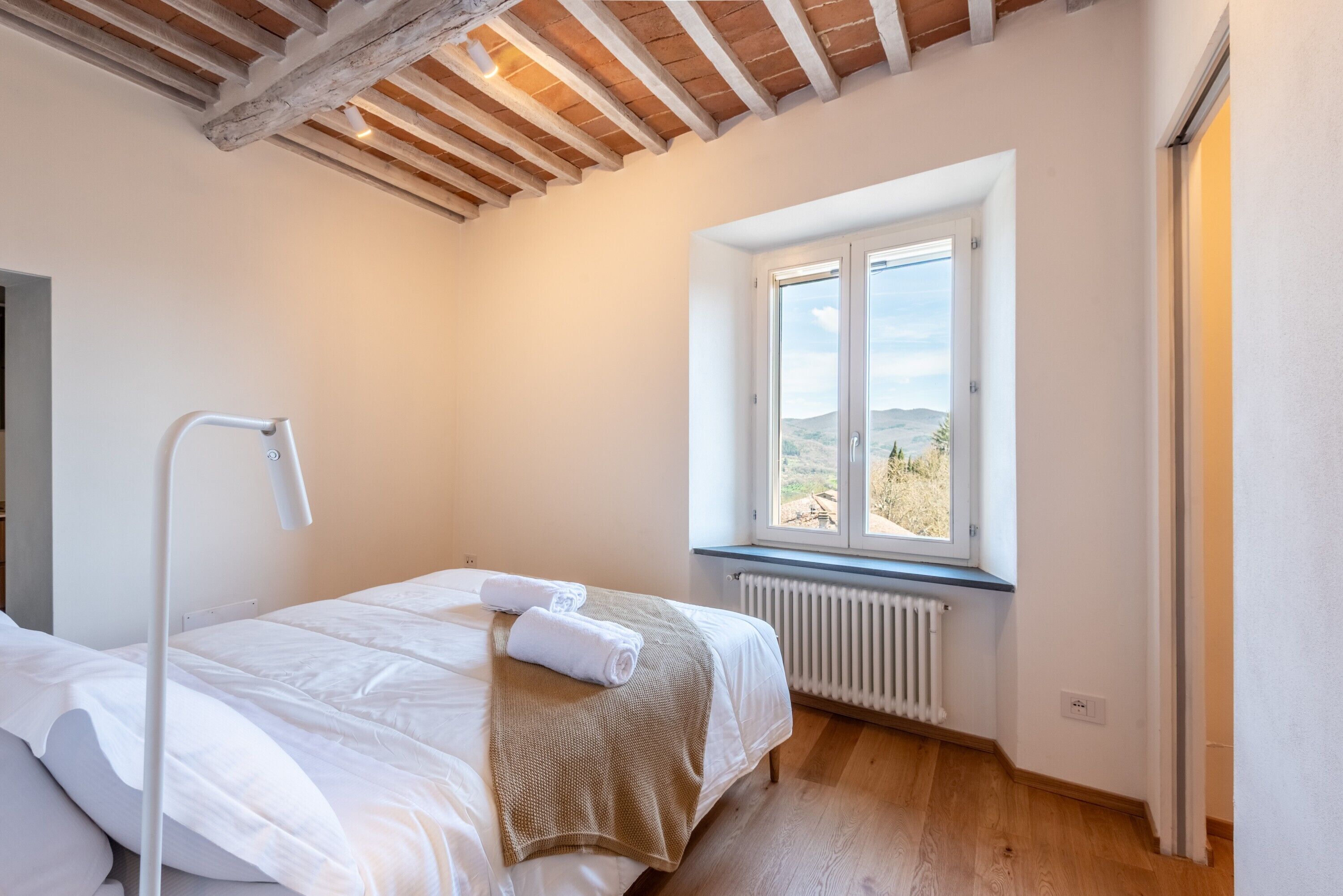 A bedroom with a bed, a window with a view, a radiator, and a wooden ceiling.