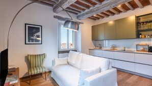 Een moderne woonkamer met een witte bank, een gestreepte stoel, een televisie en een keuken met kasten en een hanglamp.