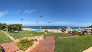 A pool area with a view of the ocean, surrounded by green lawns and a small structure. - Apartment 'Villa Elena' with Sea View, Shared Pool and Air Conditioning (Lu Bagnu)