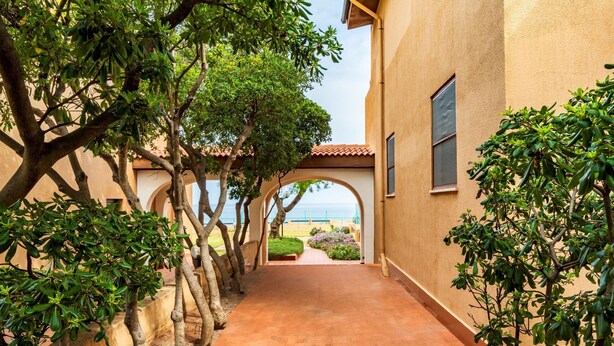 A corridor with a tiled floor, trees, and a view of the sea. - Apartment 'Villa Elena' with Sea View, Shared Pool and Air Conditioning (Lu Bagnu)