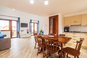 A modern kitchen with wooden cabinets, a dining table with chairs, a TV mounted on the wall, and a sliding glass door leading to an outdoor area. - Apartment 'Villa Elena' with Sea View, Shared Pool and Air Conditioning (Lu Bagnu)