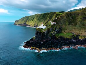 A coastal building with a lighthouse, surrounded by green hills and rocky coastline.