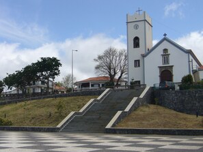 Une église dotée d’un clocher, d’un escalier menant à l’entrée et d’une zone pavée devant.