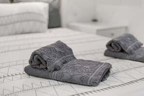 A neatly made bed with patterned bedding and rolled towels.