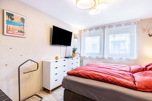 Une chambre à coucher avec un lit, un téléviseur fixé au mur, une fenêtre avec des rideaux et une affiche accrochée au mur.