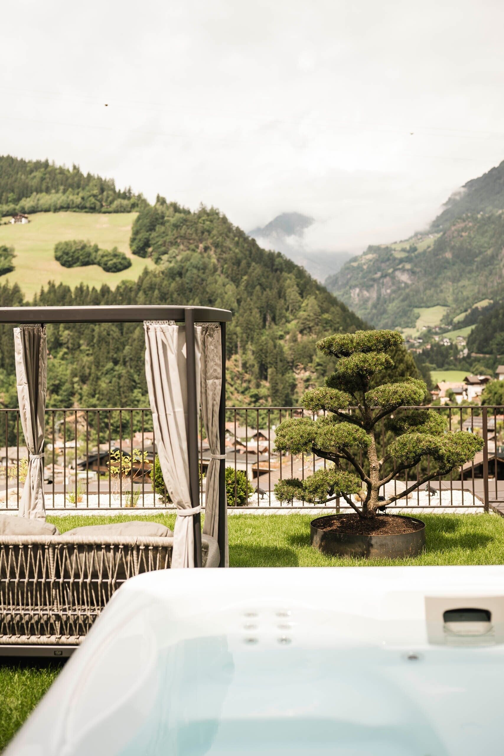 Un balcone con vista su un paesaggio montuoso, un piccolo albero e una vasca idromassaggio.