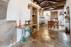 A rustic interior with a wooden table, vintage sewing machine, and a dining area with chairs and a cabinet. - Double Room 3 – Quinta do Rossio - Rural Tourism (Biscoitos)