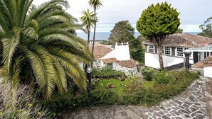A coastal building with a stone pathway, palm trees, and a view of the sea. - Double Room 3 – Quinta do Rossio - Rural Tourism (Biscoitos)