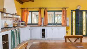 Een keuken met witte kasten, een houten bankje, een fornuis en een raam met gordijnen.