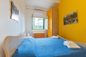 A bedroom with a bed, a window, a painting, and a wooden headboard.