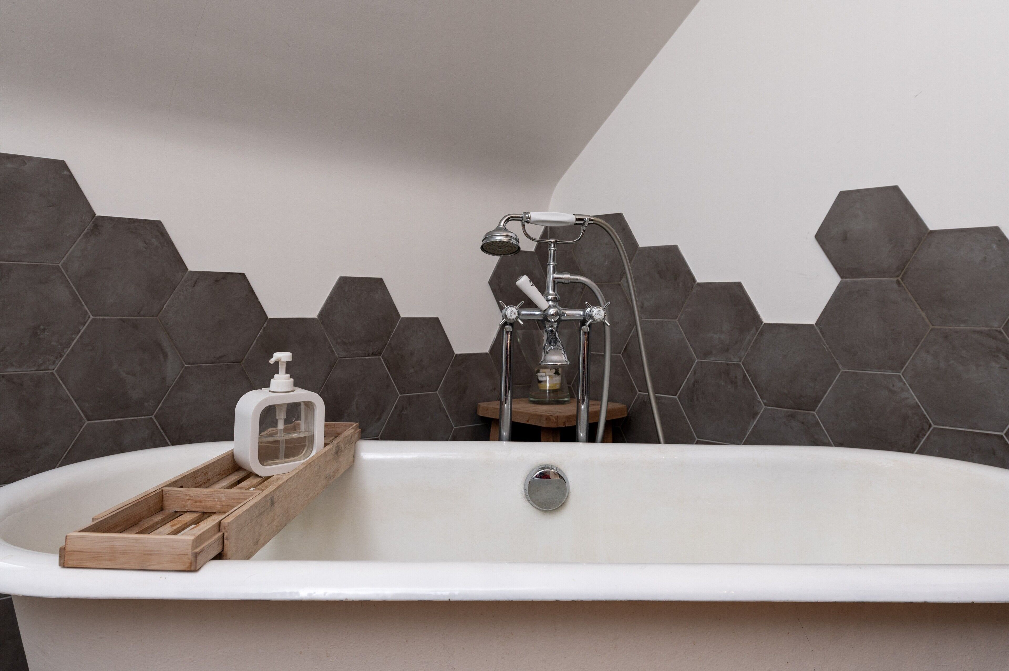 Une salle de bain moderne avec une baignoire sur pieds, une douchette et un distributeur de savon posés sur un plateau en bois.