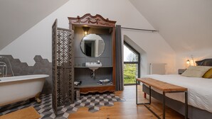 Un dormitorio con cama, un banco de madera, un baño con bañera y vistas al exterior.