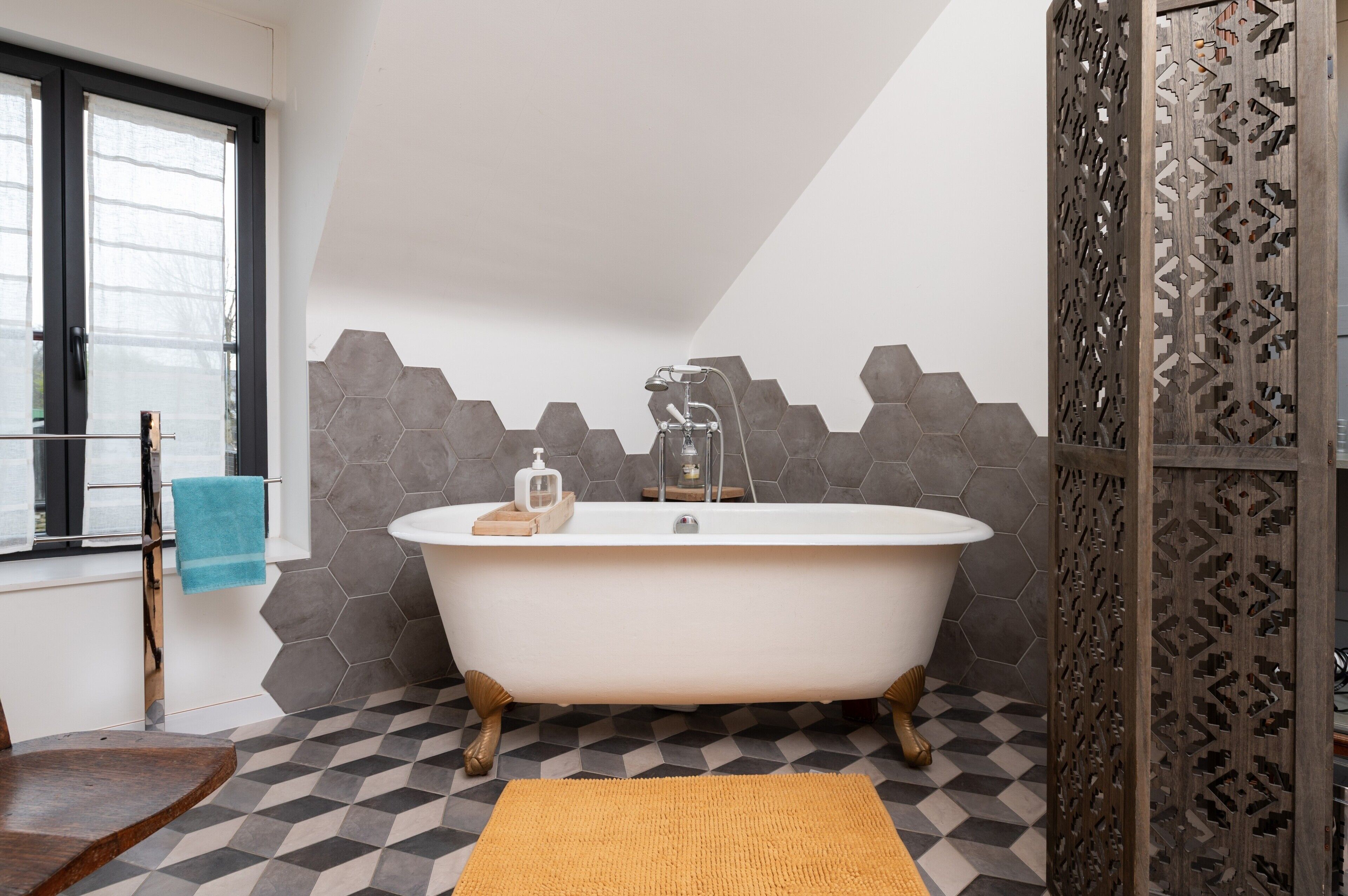 A modern bathroom with a freestanding bathtub, a window with a towel, and a geometric patterned wall.