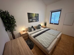 A bedroom with a bed, bedside tables, a nightstand, a window with a view, a wall-mounted painting, and a potted plant. - Stylish Apartment with Loft – Dogs Welcome (Falkenstein)