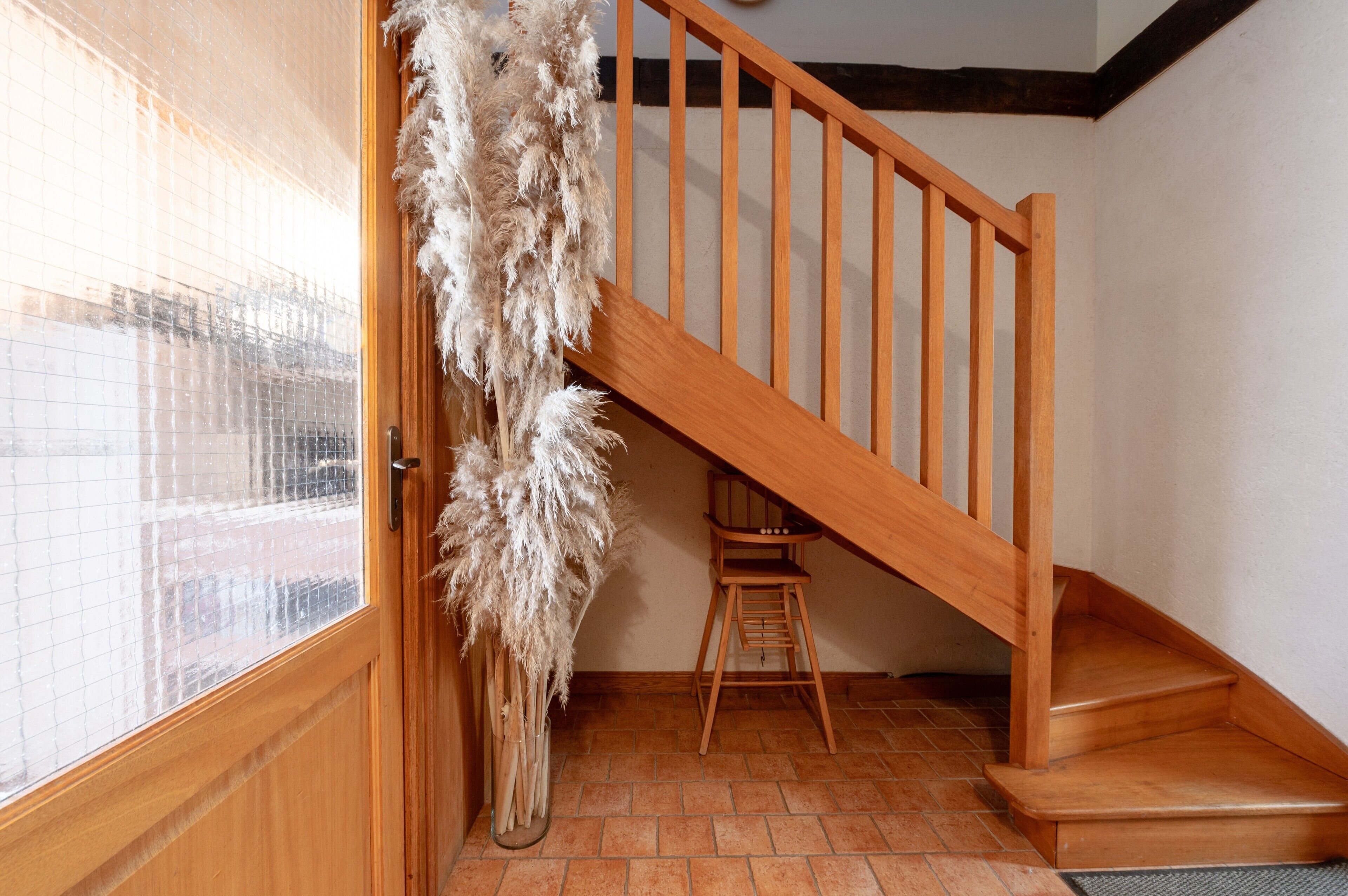 Un escalier en bois avec une chaise en bas, une porte avec une fenêtre et une plante décorative.