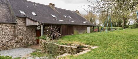 A stone building with a sloped roof, a covered porch, and a swing set in the yard.