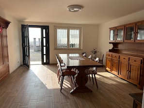 Une cuisine spacieuse avec une grande table en bois, des placards et une vue dégagée par une porte ouverte.
