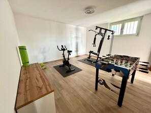 Une pièce comprenant une table en bois, un vélo d’exercice, un vélo d’appartement et une table de baby-foot.