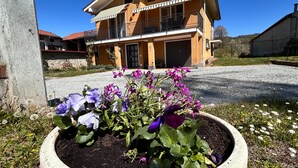 Ein zweistöckiges Gebäude mit Balkon, Kiesweg und Blumenbeet mit violetten Blumen.