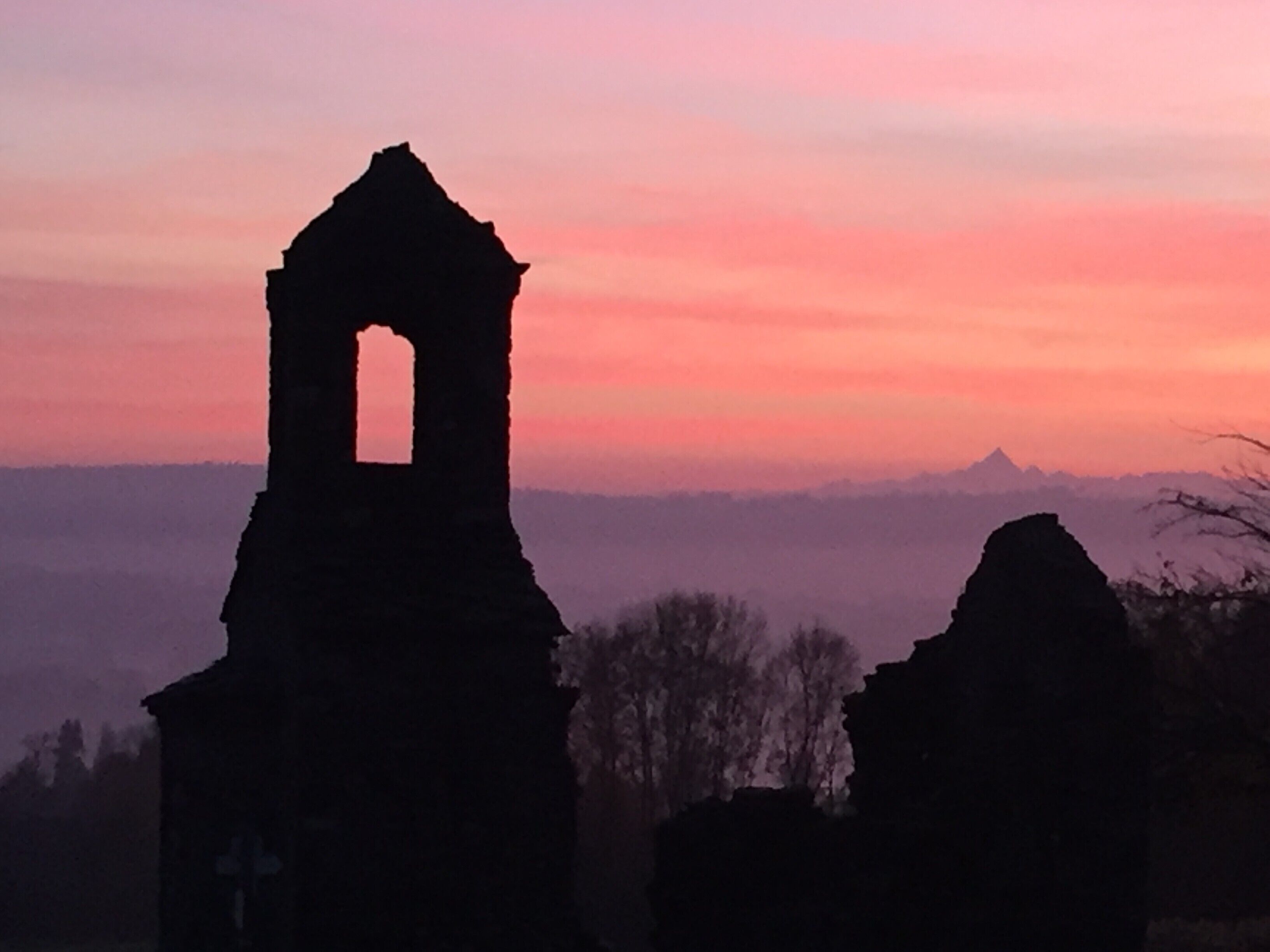 La silhouette d’un bâtiment en ruine, avec une tour centrale, se détache sur le ciel au coucher du soleil.