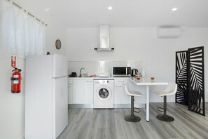 Une cuisine compacte équipée d’un lave-linge, d’un four à micro-ondes et d’un petit coin repas avec deux tabourets.
