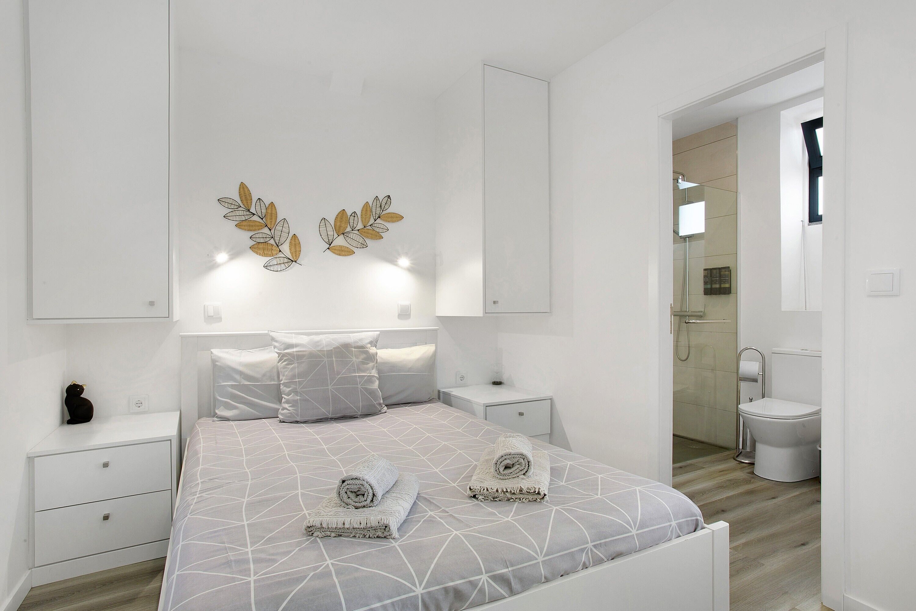 Camera da letto con un letto, due comodini, una lampada a parete e un bagno visibile attraverso una porta aperta.