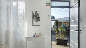 Una habitación con un tocador blanco, una obra de arte enmarcada, una planta en maceta y una puerta que da al exterior.