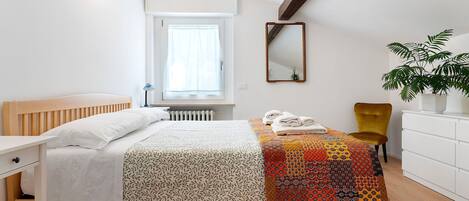 Une chambre à coucher avec un lit, une chaise, une commode, une fenêtre avec des rideaux, un miroir et une plante.