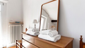 Une commode en bois avec un miroir, deux serviettes, une lampe et un radiateur, dans une pièce aux murs blancs.