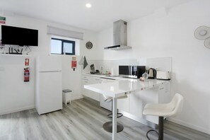 A modern kitchen with white cabinetry, a stainless steel range hood, a microwave, and a small island with bar stools. - Casa Pereira 5: Relaxing Studio for 2 Guests in Ponta do Pargo (Ponta do Pargo)