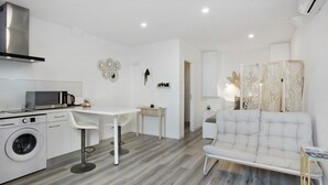 A modern kitchen with a washing machine, a dining area with a table and chairs, and a living area with a sofa and decorative panels. - Casa Pereira 5: Relaxing Studio for 2 Guests in Ponta do Pargo (Ponta do Pargo)
