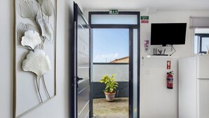 A hotel room with a sliding door leading to a balcony, a mounted television, a fire extinguisher, and a framed artwork on the wall. - Casa Pereira 5: Relaxing Studio for 2 Guests in Ponta do Pargo (Ponta do Pargo)