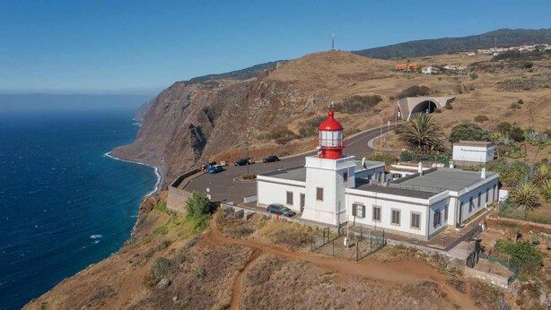 A coastal lighthouse with a white building and red top, situated on a hillside with a road leading to it. - Casa Pereira 5: Relaxing Studio for 2 Guests in Ponta do Pargo (Ponta do Pargo)