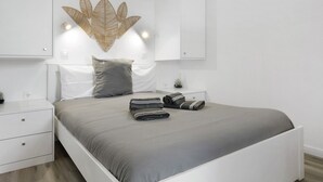 A modern bedroom with a bed, nightstands, a wall-mounted light fixture, and a decorative wall piece. - Casa Pereira 5: Relaxing Studio for 2 Guests in Ponta do Pargo (Ponta do Pargo)