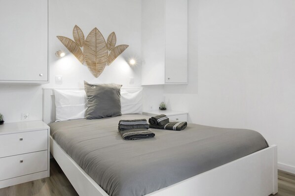 A modern bedroom with a bed, nightstands, a wall-mounted light fixture, and a decorative wall piece.