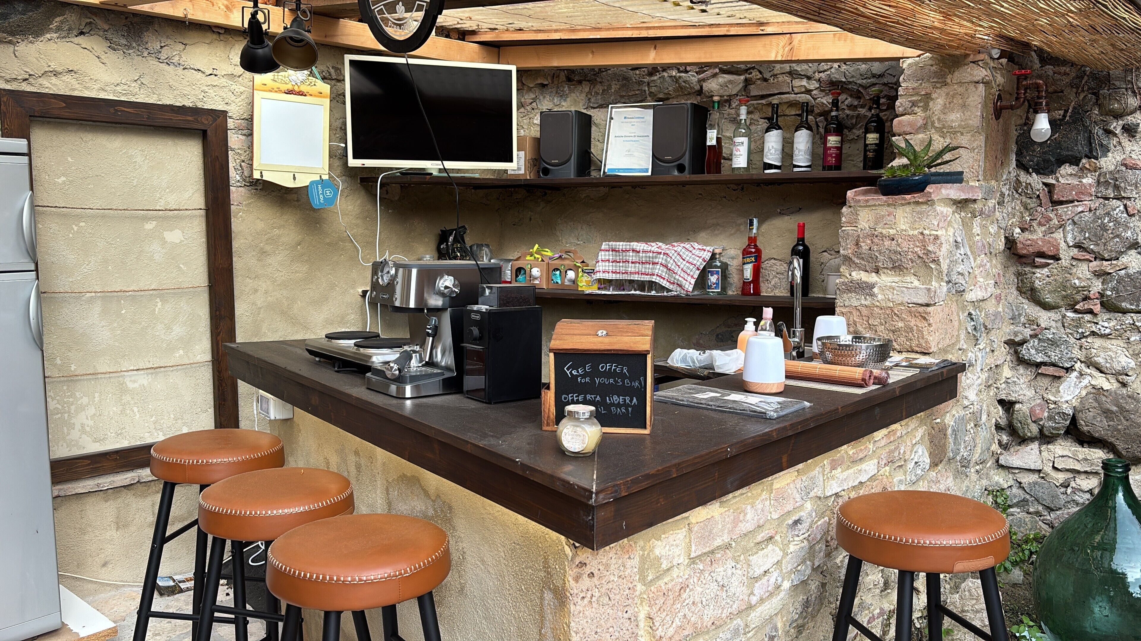 Una zona de bar con una máquina de café, taburetes, un cartel de pizarra y varias botellas.
