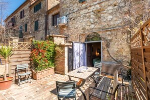 Un edificio in pietra con tavolo e sedie di legno, un piccolo giardino e una recinzione di legno.